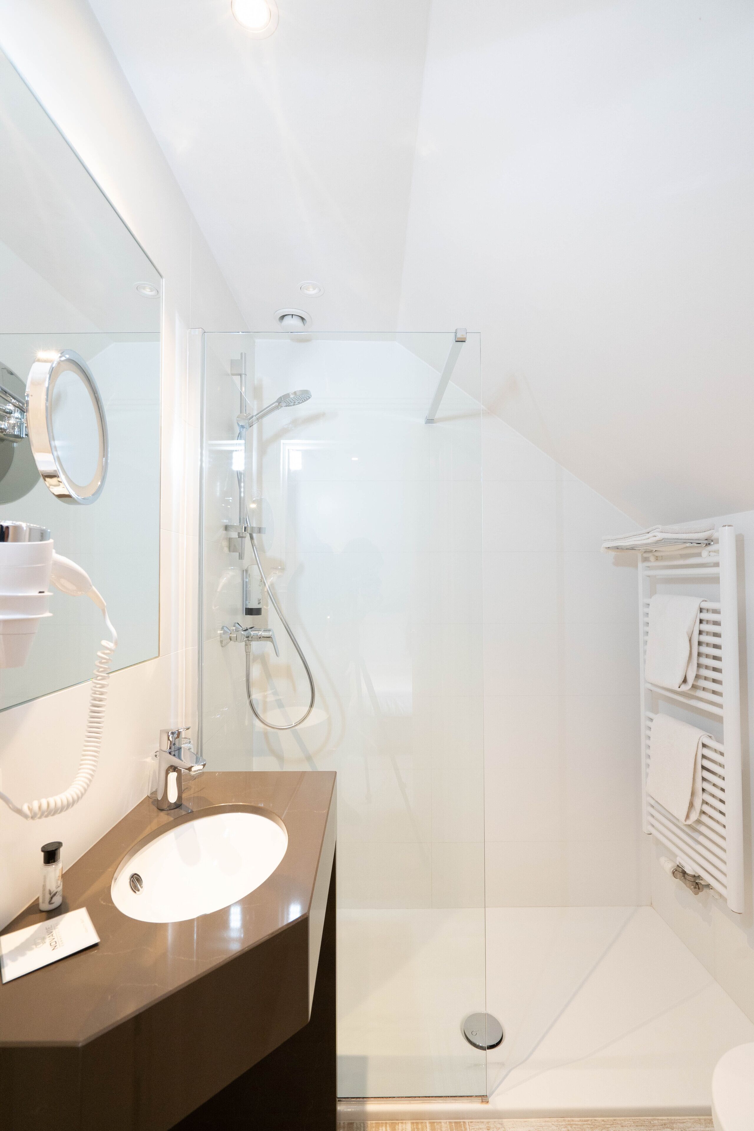 Un baño moderno con ducha envuelta en vidrio, un tocador con espejo y un perchero para toallas.