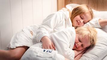 Twee personen in witte gewaden liggen in bed met een houten hoofdeinde en witte muren.
