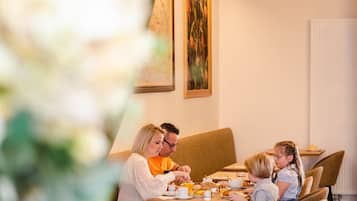 A family dining at a table with breakfast items, in a room with a radiator and framed artwork on the wall.
