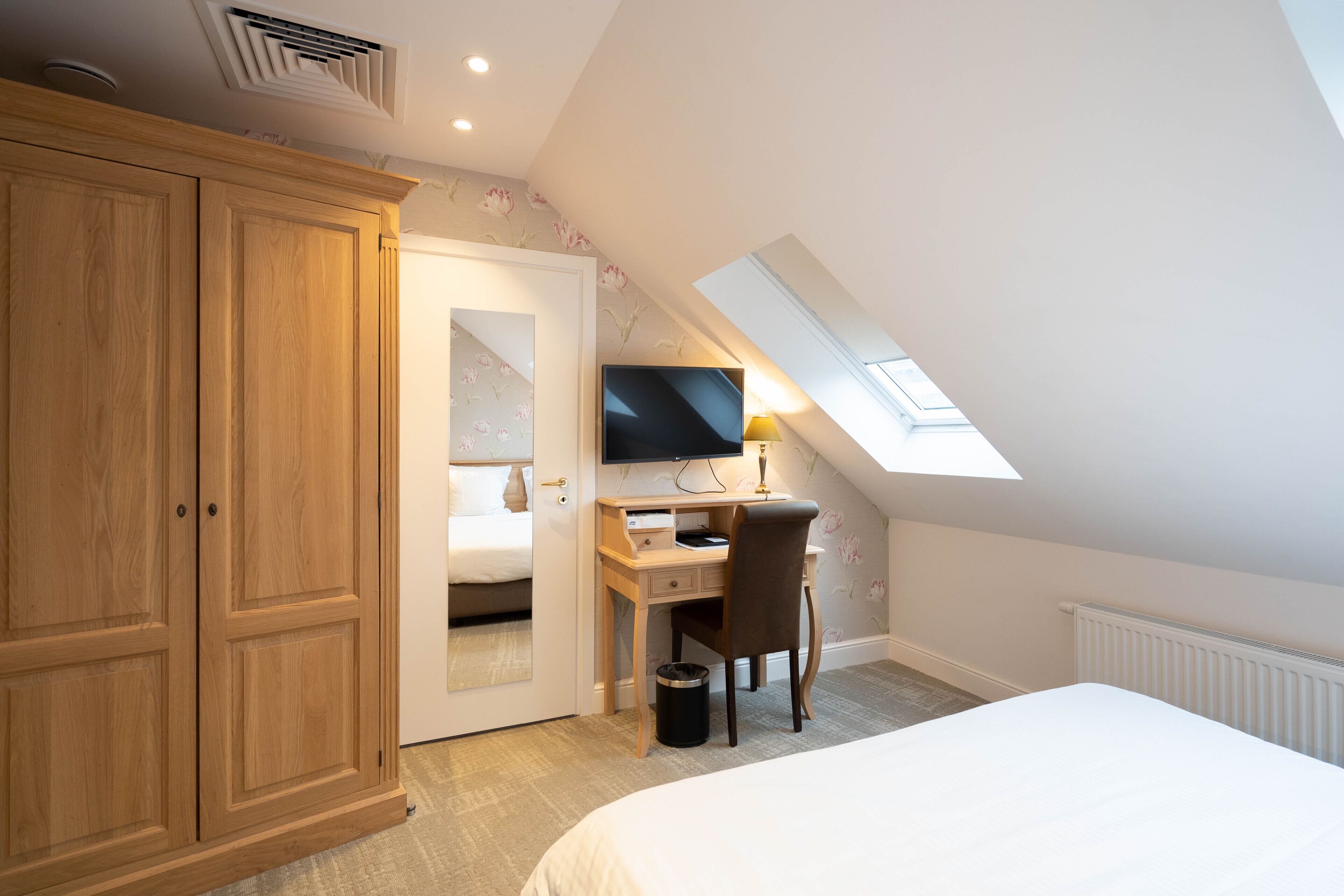 Une chambre avec une grande armoire, un bureau avec une chaise, un lit et une fenêtre de toit.