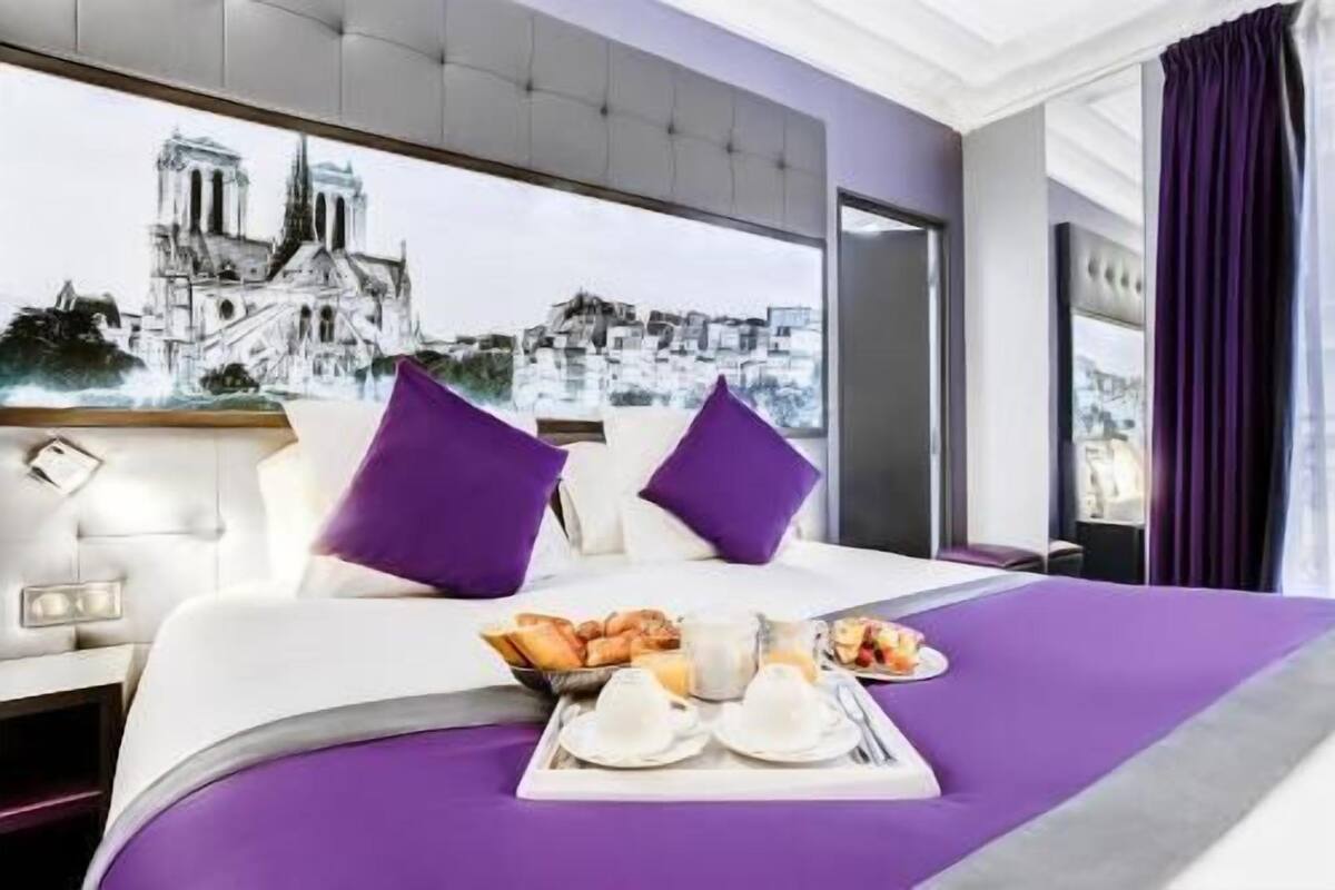 Una habitación de hotel con cama, una bandeja de desayuno y un amplio ventanal con vista a la ciudad.