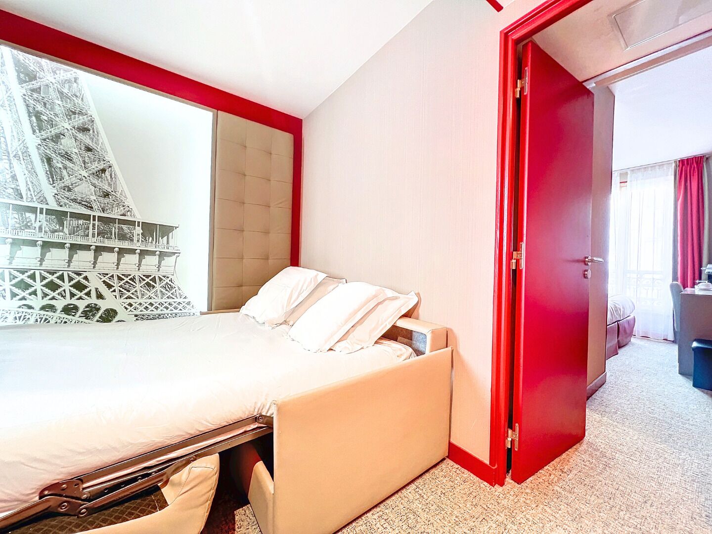 Habitación de hotel con cama, una puerta roja y vista de la Torre Eiffel.