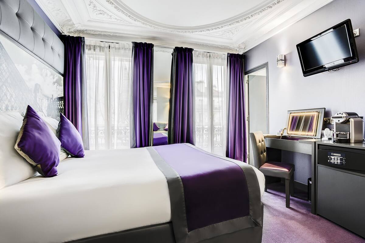 Habitación de hotel con una cama grande, un escritorio con una silla, un televisor y un minibar.