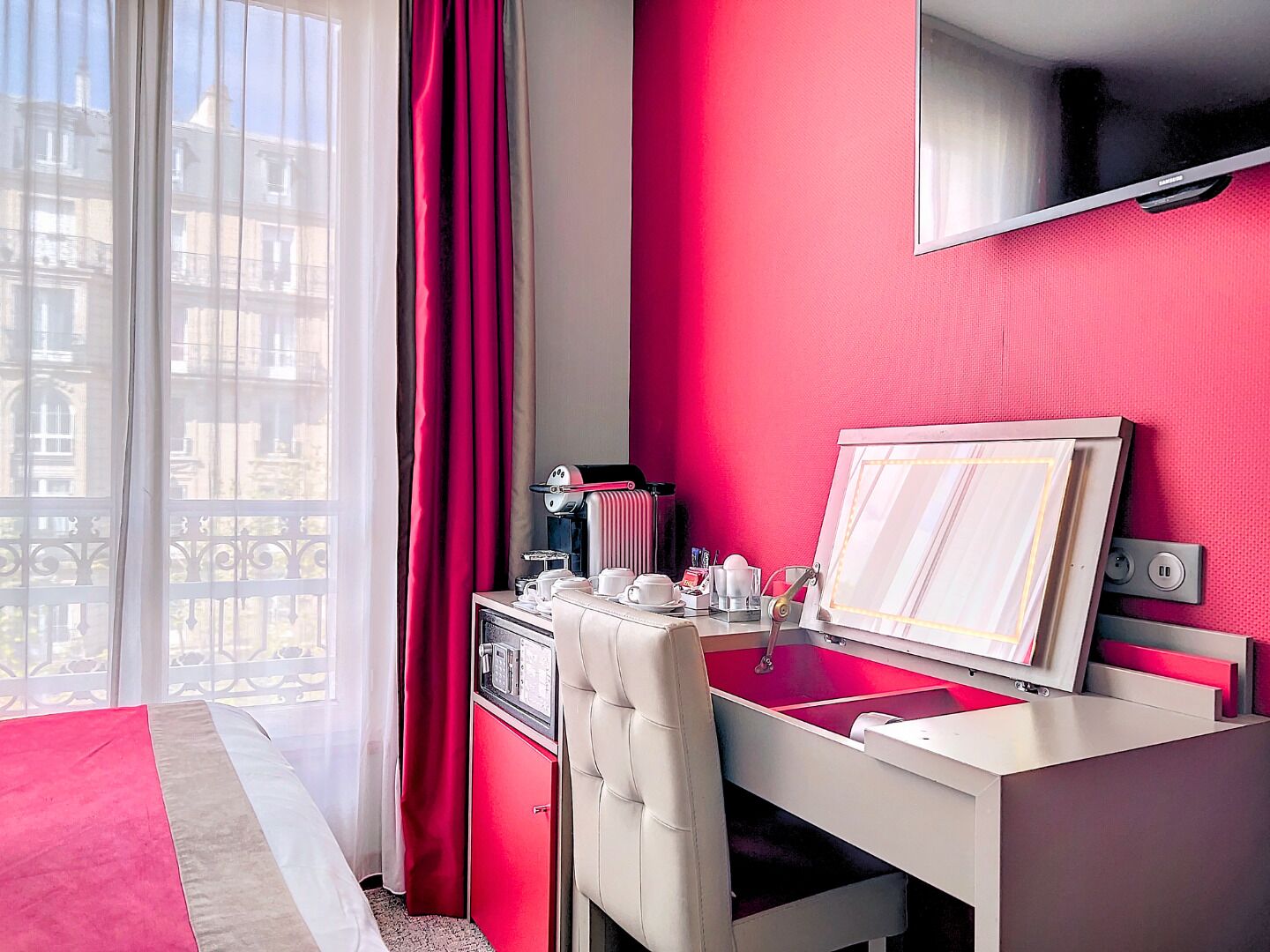 Une chambre d’hôtel comprenant un lit, un bureau avec une chaise, une télévision et une fenêtre avec des rideaux.