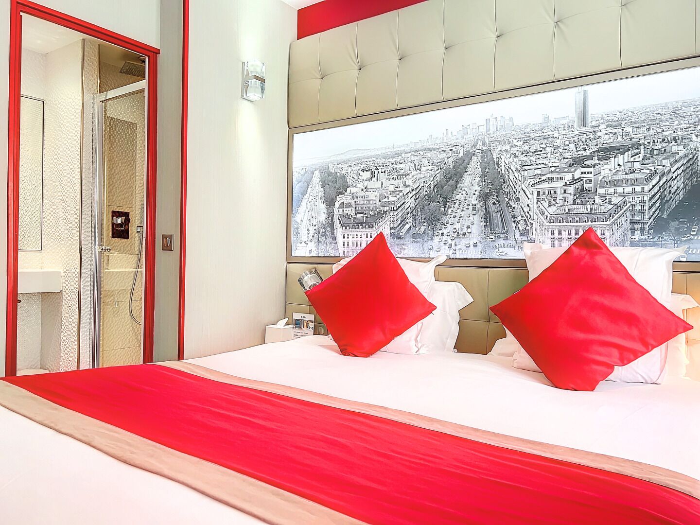 Une chambre d’hôtel avec un grand lit, deux oreillers rouges, une vue sur la ville et un mur d’accent rouge.