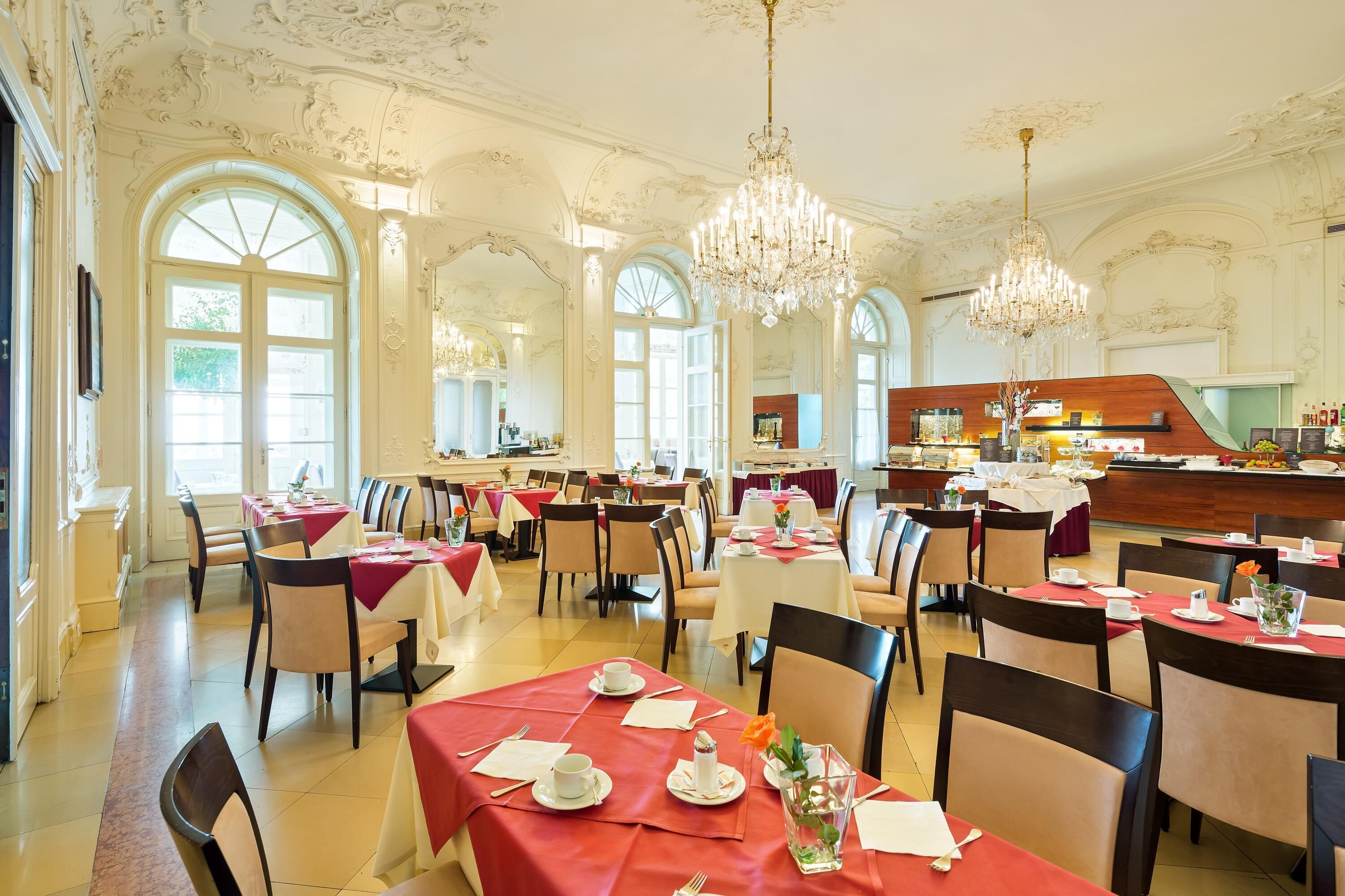A grand dining hall with ornate ceilings, chandeliers, and a central bar area.