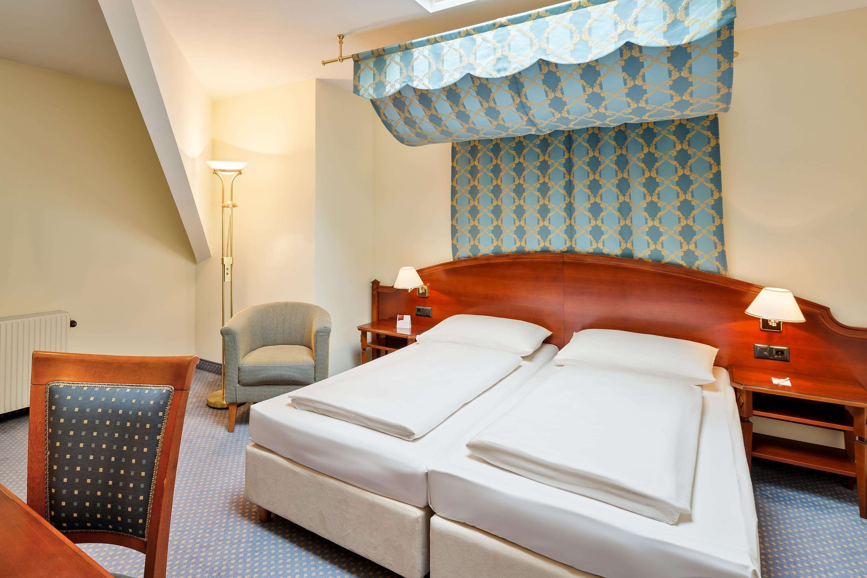 Ein Hotelzimmer mit einem Doppelbett, zwei Nachttischen mit Lampen, einem Sessel und einer Wand mit Muster.