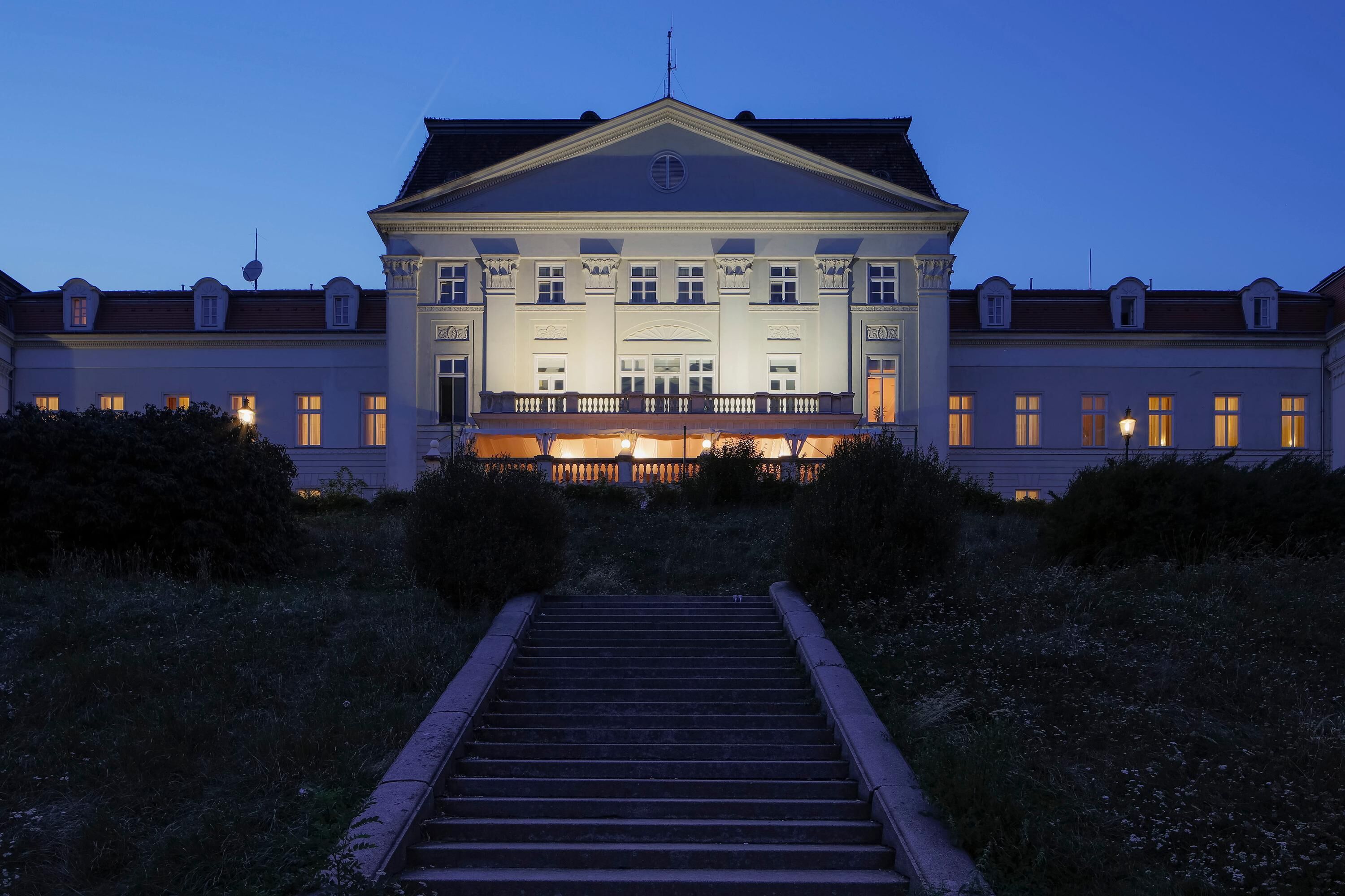 A grand building with a symmetrical facade, large windows, and a central entrance with a staircase leading up.