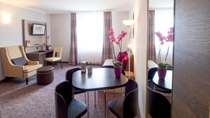 Hotelkamer met een zithoek, een bank, een kleine tafel met stoelen, een televisie en een potplant.