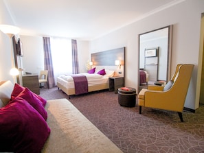 A hotel room with a bed, a sofa, a chair, a desk, and a mirror. - Arion Cityhotel Vienna (Vienna)