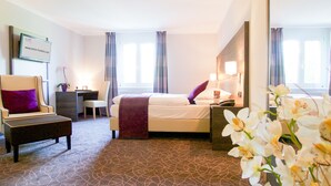 Een hotelkamer met een bed, een stoel, een bureau, een nachtkastje en een spiegel.