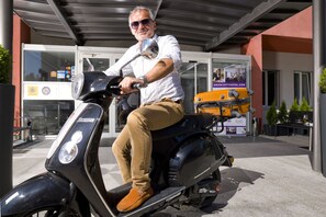 A man on a scooter in front of a building with a glass facade and a sign for a hotel. - Arion Cityhotel Vienna (Vienna)