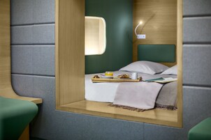 A compact, modern room with a bed, bedside table, and a small window.