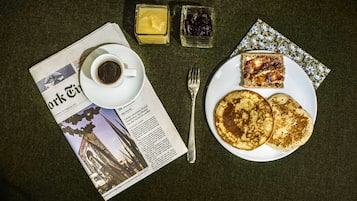 Desayuno con tortitas, café y salsas sobre una mesa con un periódico.
