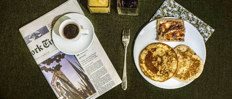A breakfast setting with pancakes, coffee, and condiments on a table with a newspaper.