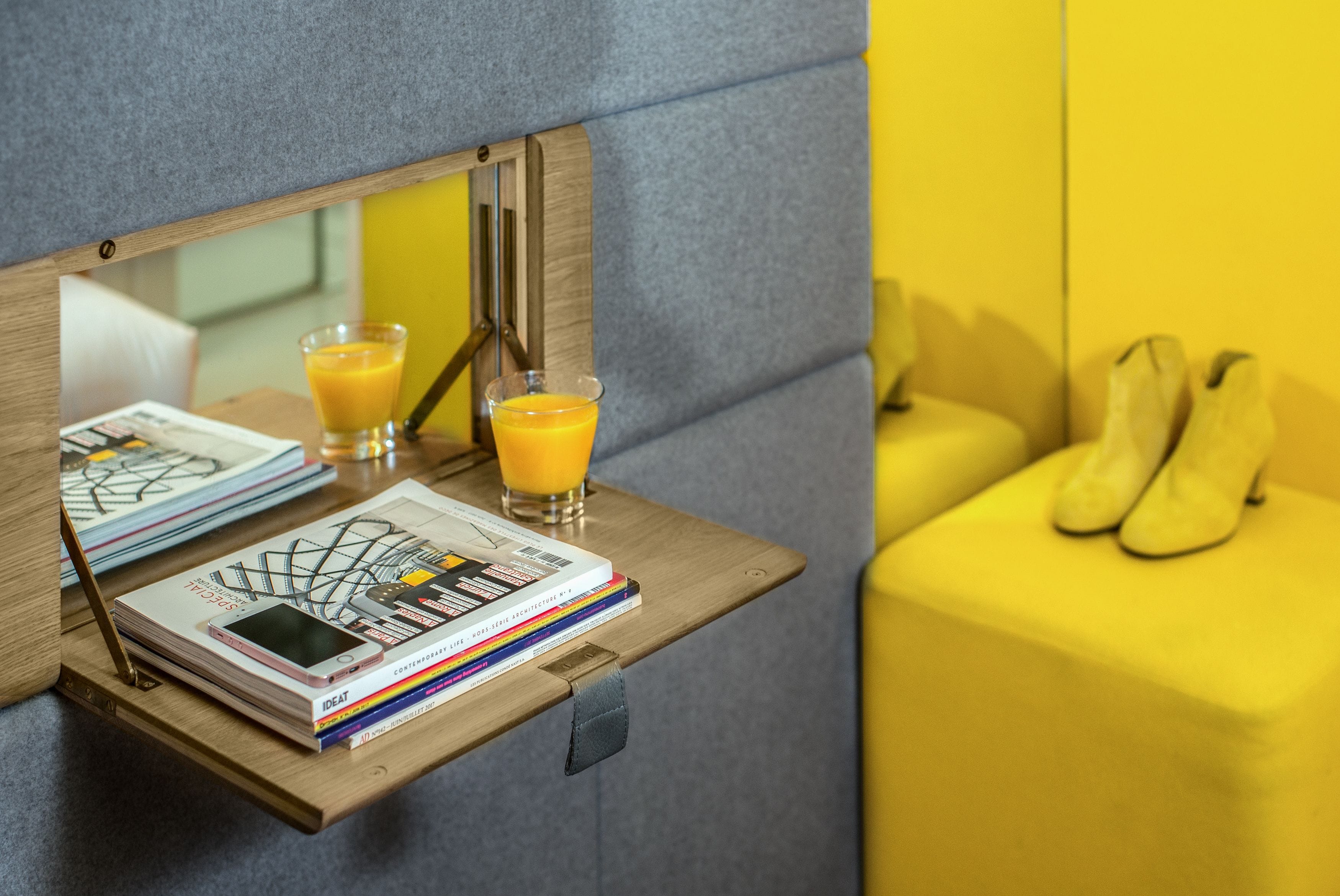 A wooden side table with a smartphone, magazines, and a glass of orange juice.