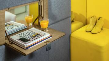 A wooden side table with a smartphone, magazines, and a glass of orange juice.