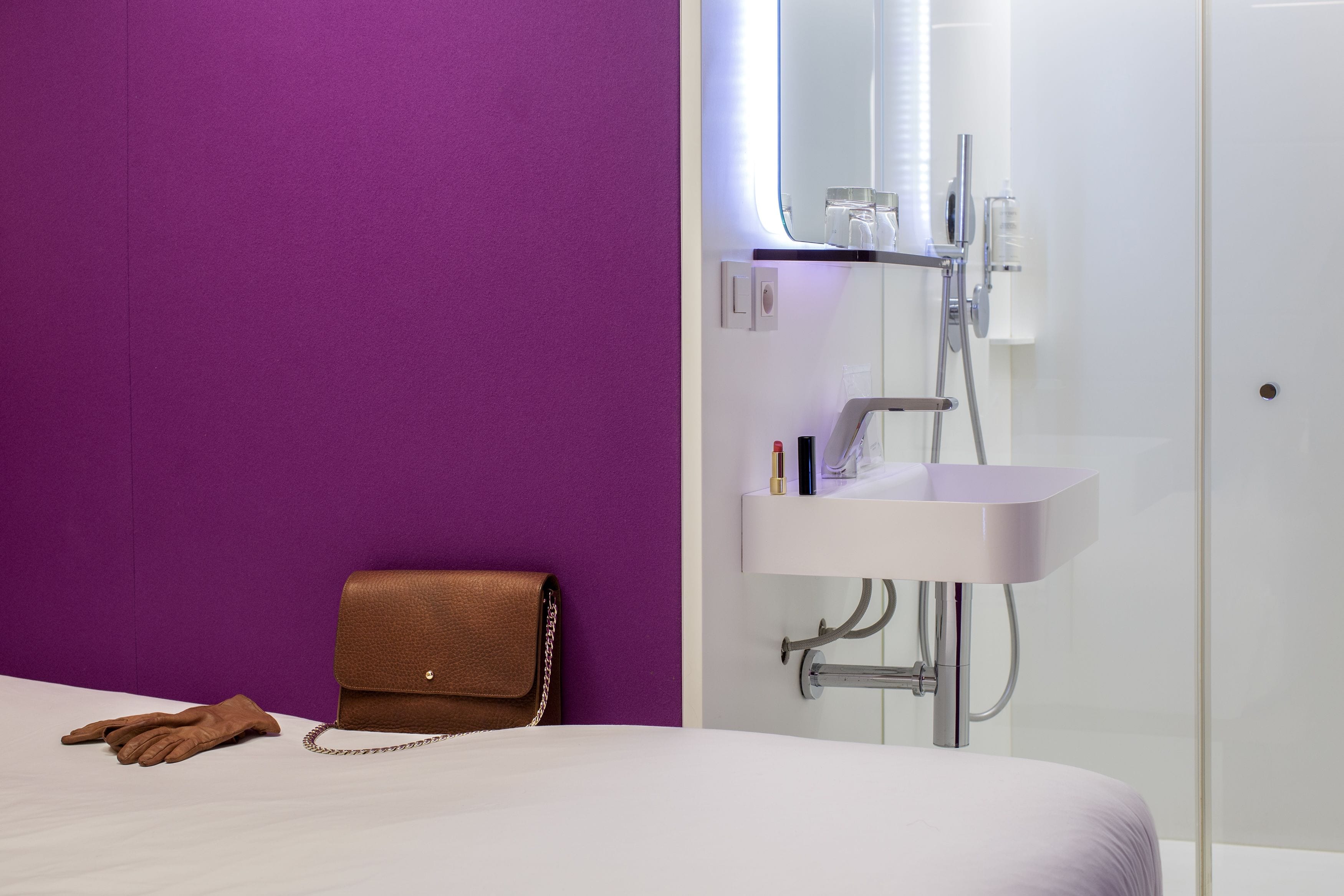 A modern bathroom with a purple wall, a white sink, and a brown handbag on the floor.
