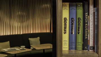 Una estantería con libros titulados 'domus' y 'water & seek' en una habitación de diseño moderno, que incluye un sofá y una mesa.