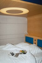 A hotel room with a bed, a hanging light fixture, a bedside table, and a wall-mounted control panel.
