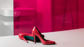 Ein modernes Badezimmer mit Duschabtrennung, einem weißen Waschbecken und einem Paar roter High Heels auf einer weißen Oberfläche.