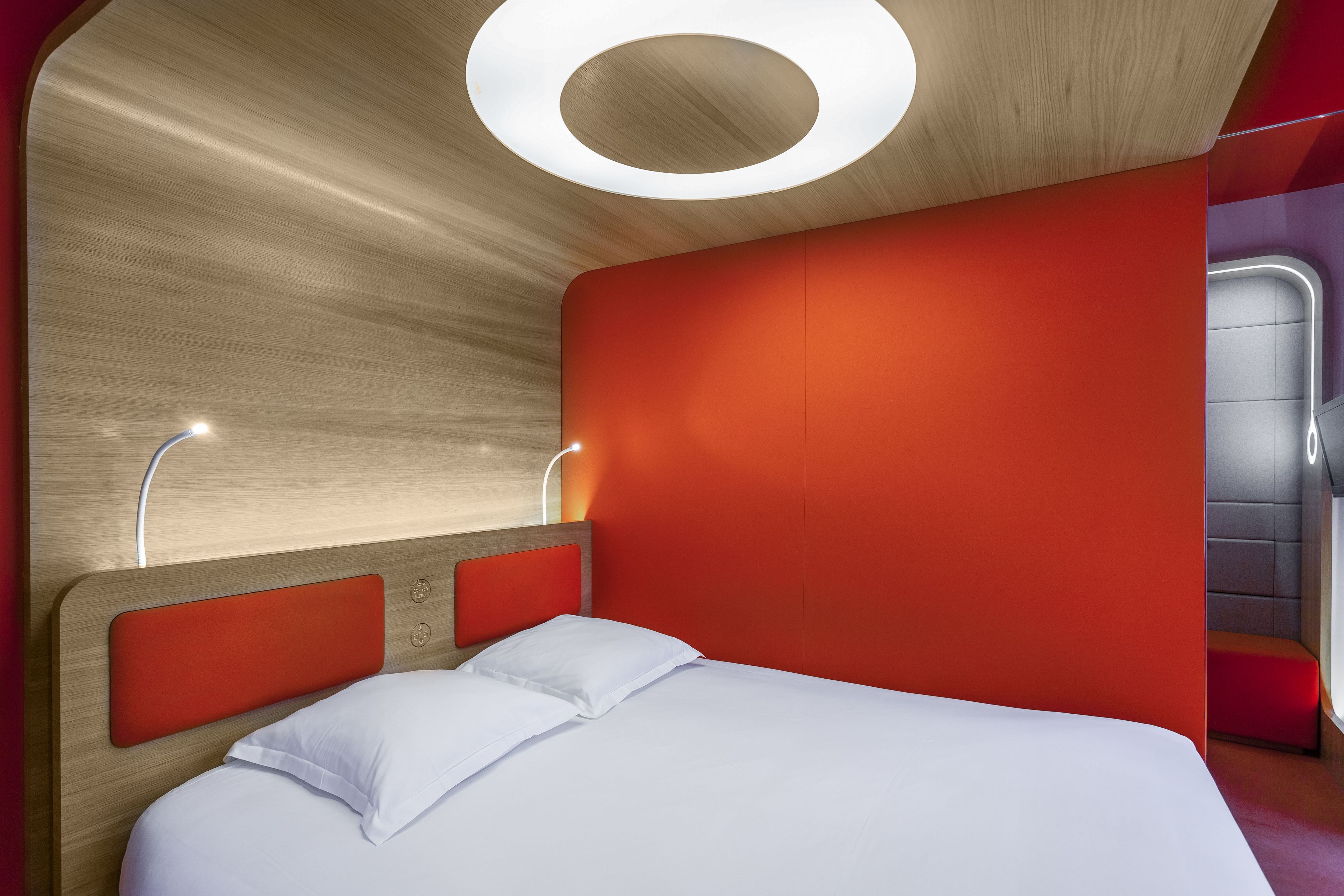 Een moderne hotelkamer met een houten hoofdbord, een rode accentmuur en een groot bed met witte lakens.
