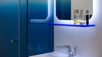 Un baño con mampara de vidrio, un lavabo blanco y un estante azul con artículos de aseo.