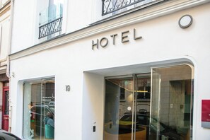A hotel entrance with a glass door, a visible car parked outside, and a sign above the door. - Hotel Odyssey (Paris)