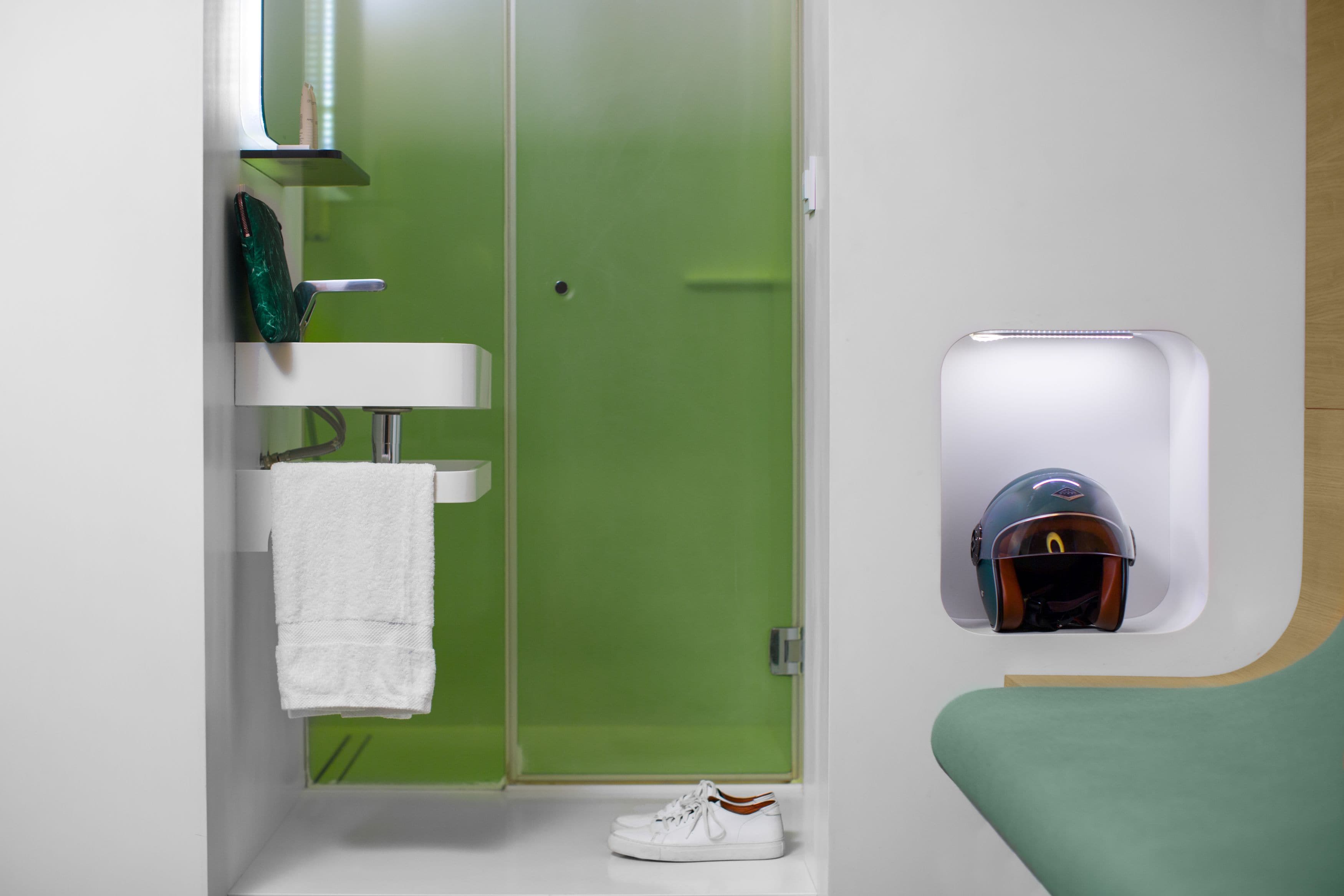 Um banheiro com porta verde, pia branca e uma toalha pendurada na parede.