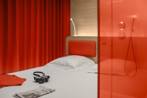 A hotel room with a bed, a camera, and a red curtain.