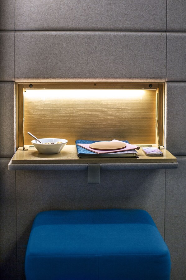 A small, enclosed space with a wooden shelf holding a bowl, a notebook, and a smartphone.