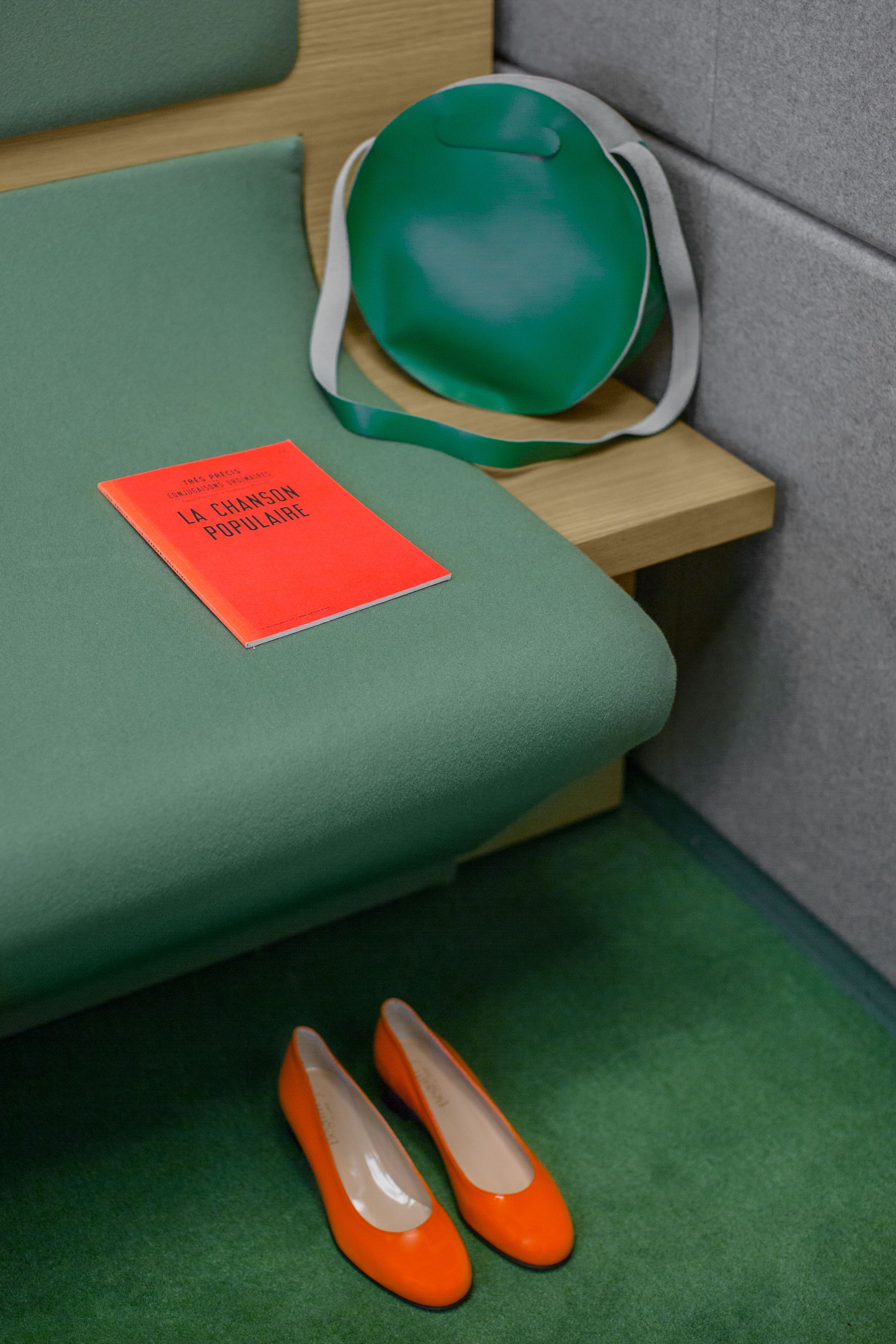 A green upholstered seat with a red book titled "LA CHANGON POPULAIRE" and a pair of orange shoes on the floor.