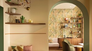 Un espacio de sala cómodo con un sofá, un sillón y una mesa de centro de madera. Hay estantes con adornos y una biblioteca llena de libros y plantas.