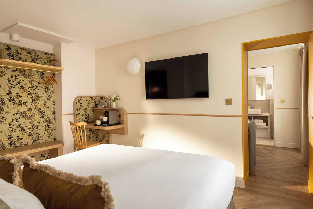 A hotel room with a bed, a desk with a chair, a television, and a mirror.