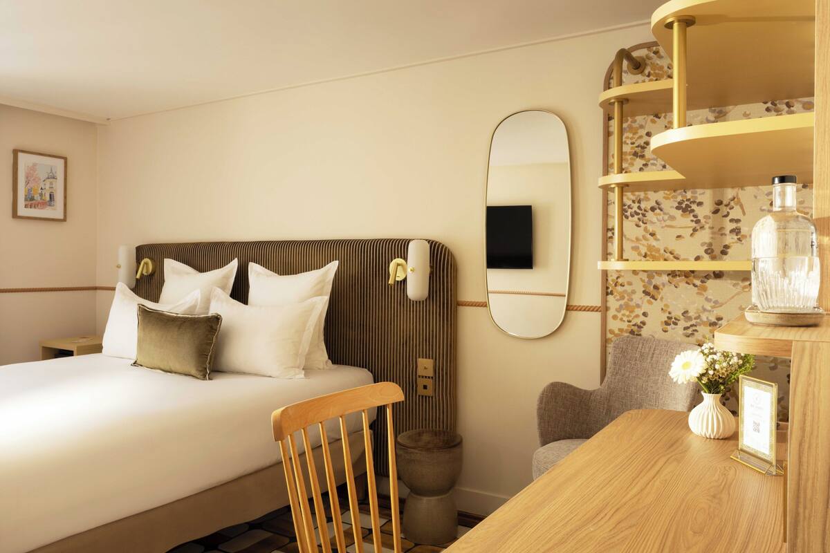 A hotel room with a bed, a wooden chair, a small table, a mirror, and a decorative shelf.