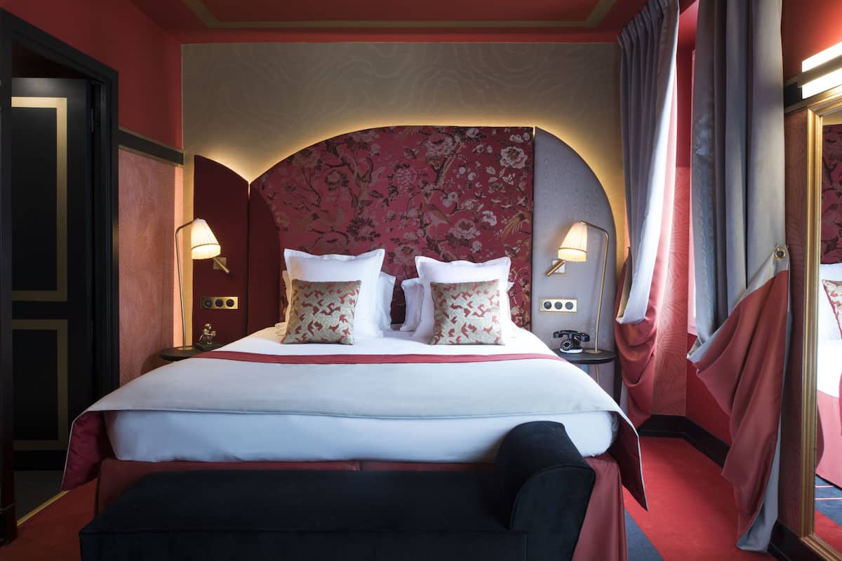 A hotel room with a large bed, two bedside lamps, a red carpet, and a mirror.