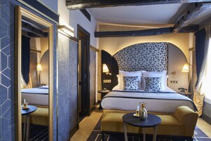 Une chambre d’hôtel avec un grand lit, deux tables de chevet, une petite table ronde et un miroir.