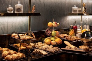 Un buffet proposant une variété de pains, de viennoiseries, de fruits et de boissons.