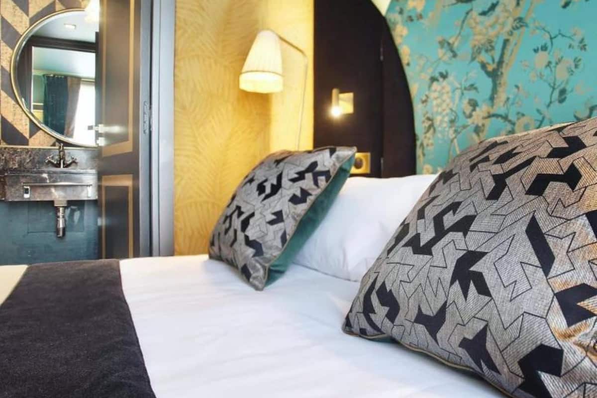 A hotel room with a bed, a mirror, a sink, and a wall with a floral pattern.