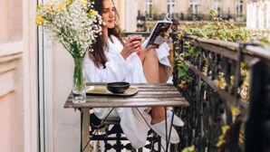 A person sitting at a table with a book, on a balcony with a view of buildings. - Maison Nabis by Happyculture (Paris)