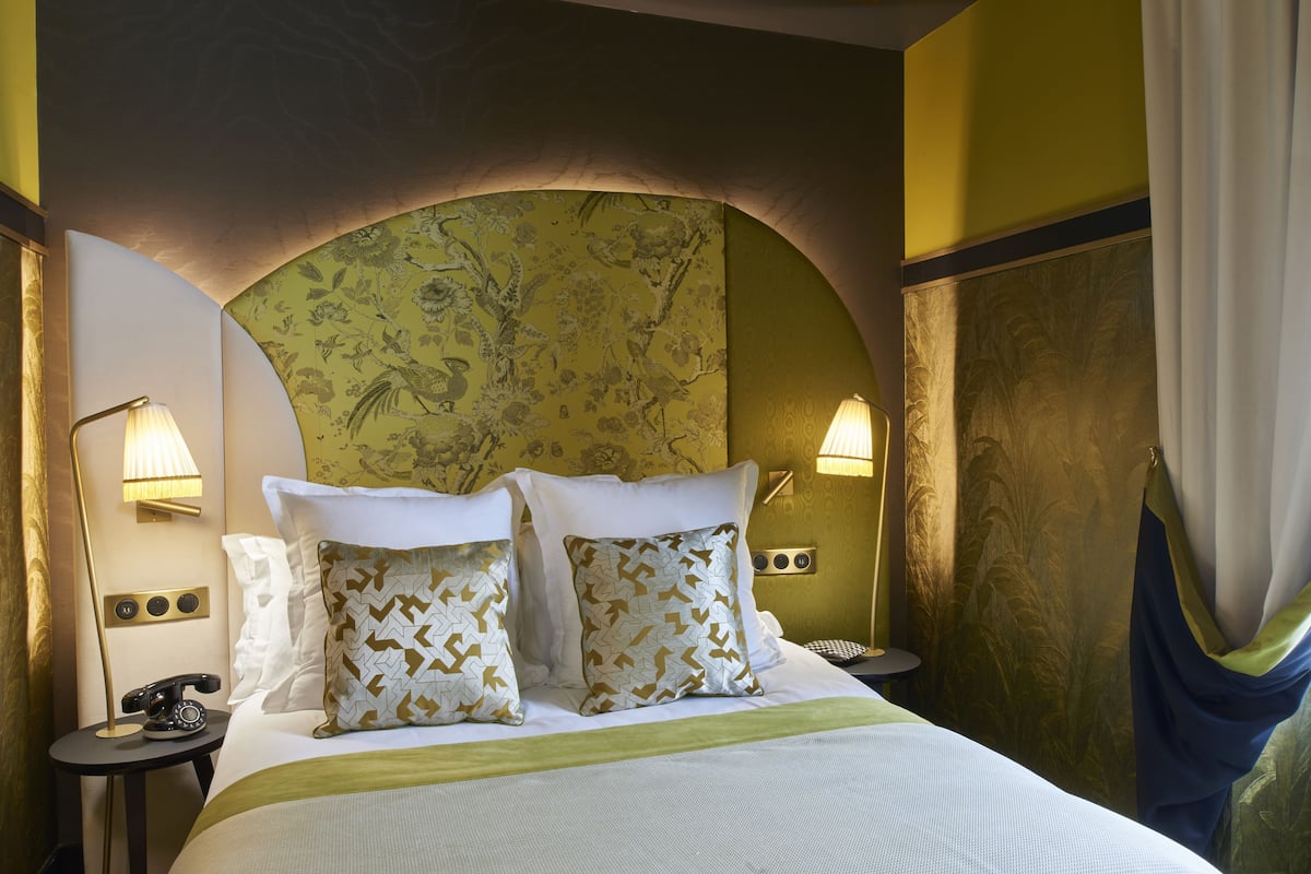A hotel room with a large bed, two bedside lamps, a telephone, and a decorative headboard.