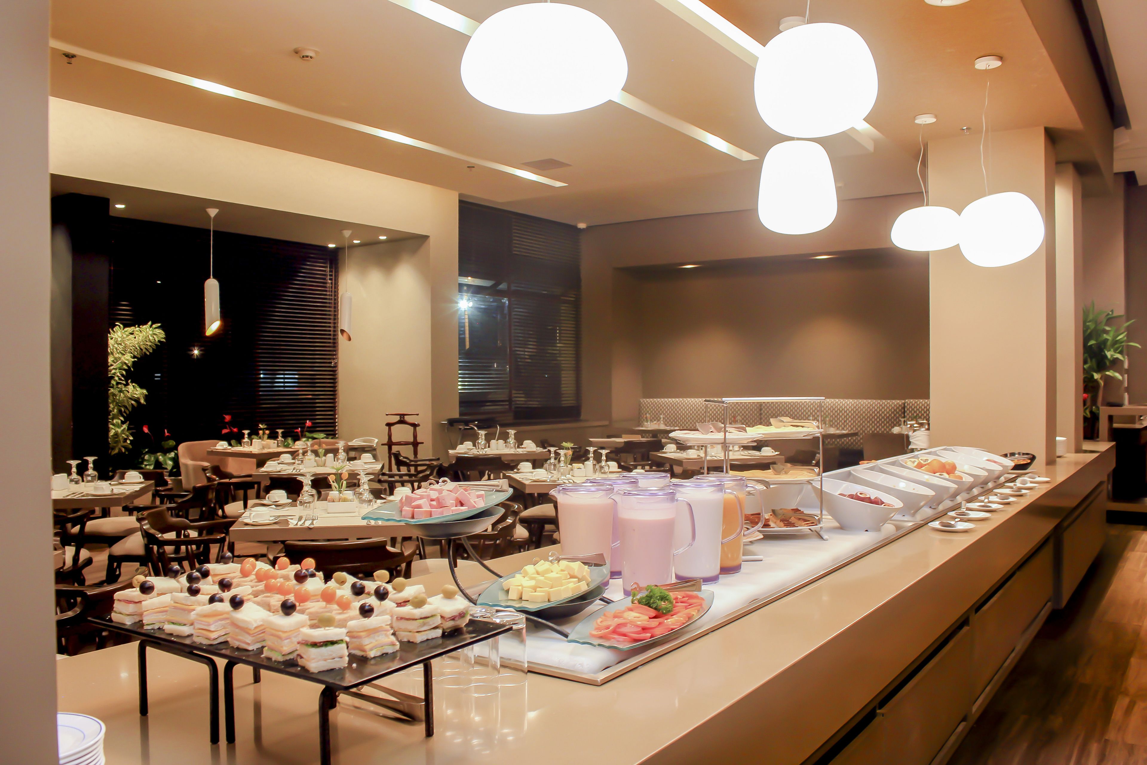 Un buffet proposant une variété de plats et de boissons, un espace repas avec des tables et des chaises, et un éclairage moderne.
