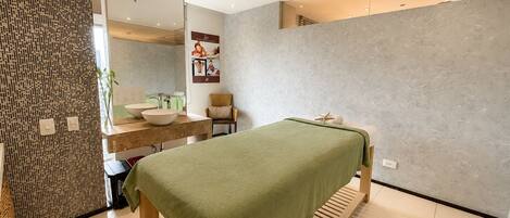 A modern spa room with a wooden bed, a large mirror, a sink, and a wall-mounted cabinet.