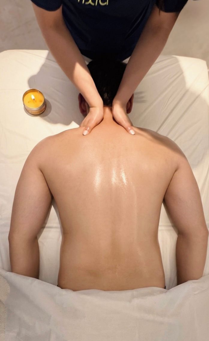 A person receiving a back massage on a bed with a candle.
