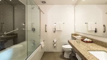Un baño moderno con ducha de vidrio, inodoro blanco y encimera de granito con artículos de aseo.