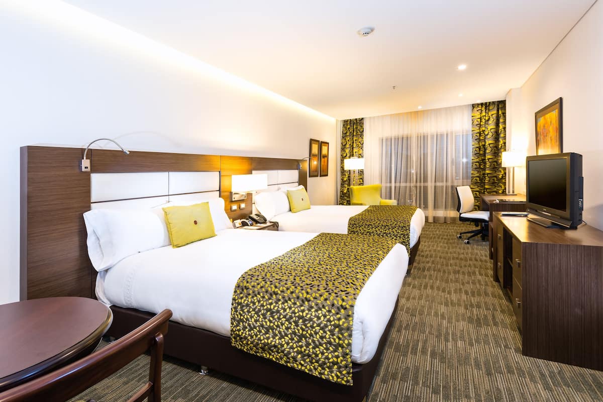 A hotel room with two beds, a desk, a TV, and a chair.