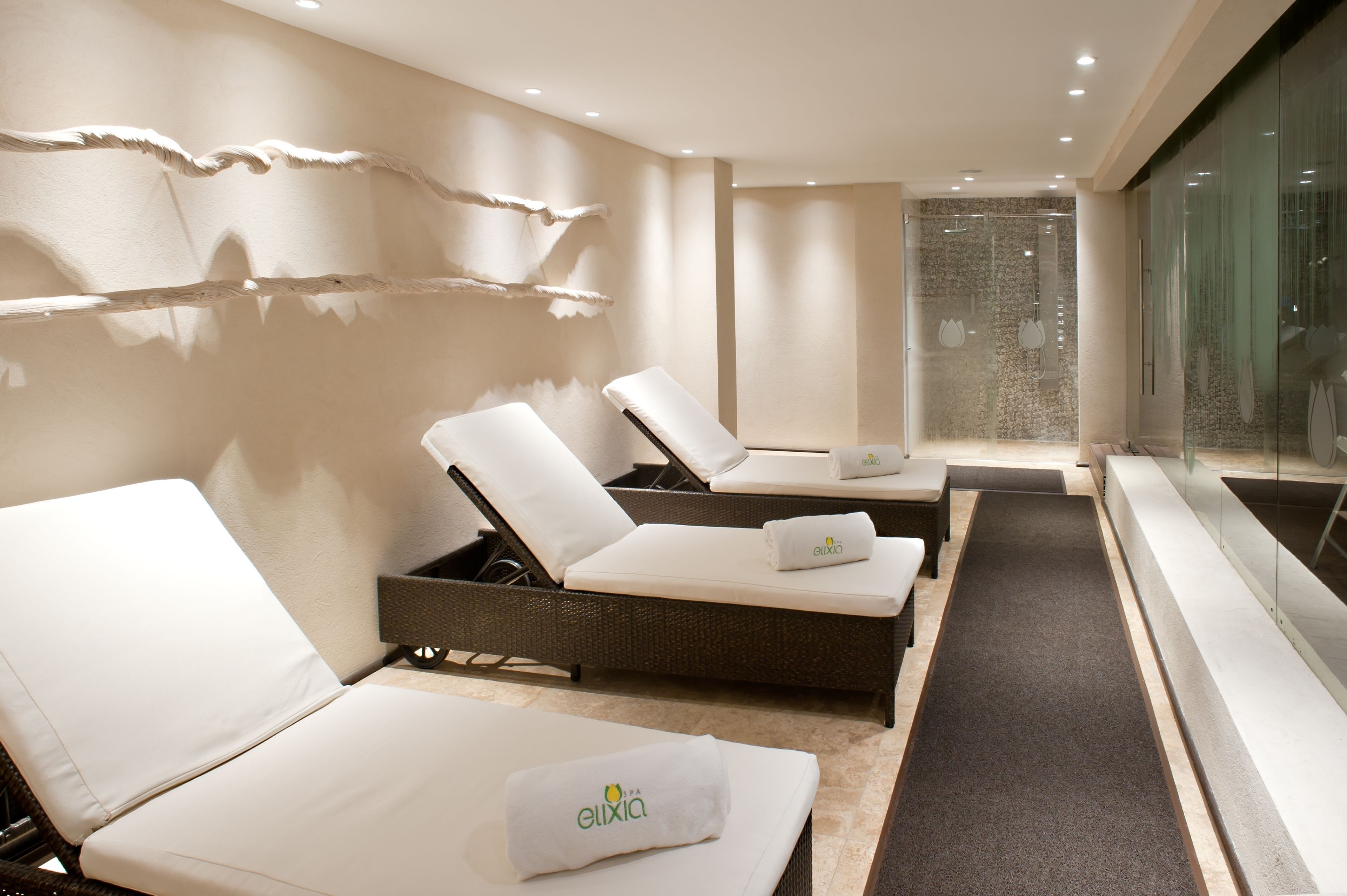 A modern spa room with three lounge chairs, a glass-enclosed shower, and a minimalist design.