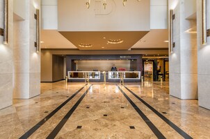 A hotel reception area with a marble floor, reception desk, and a large 'D' logo on the ceiling.