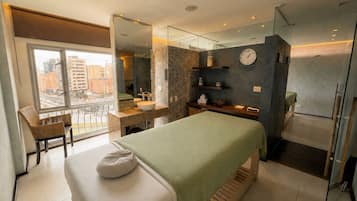 Un dormitorio moderno con cama, un rincón de descanso con sillón, un ventanal grande y un baño con lavamanos y espejo.