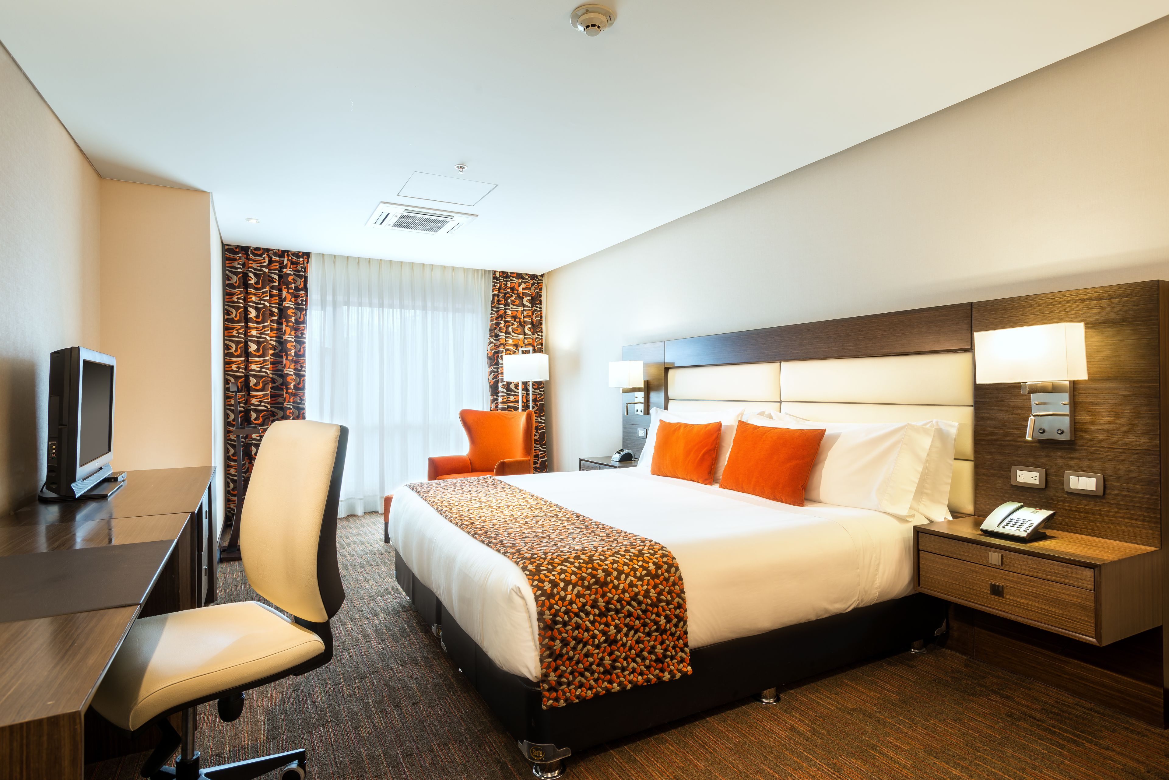 A hotel room with a bed, desk, chair, and a television.